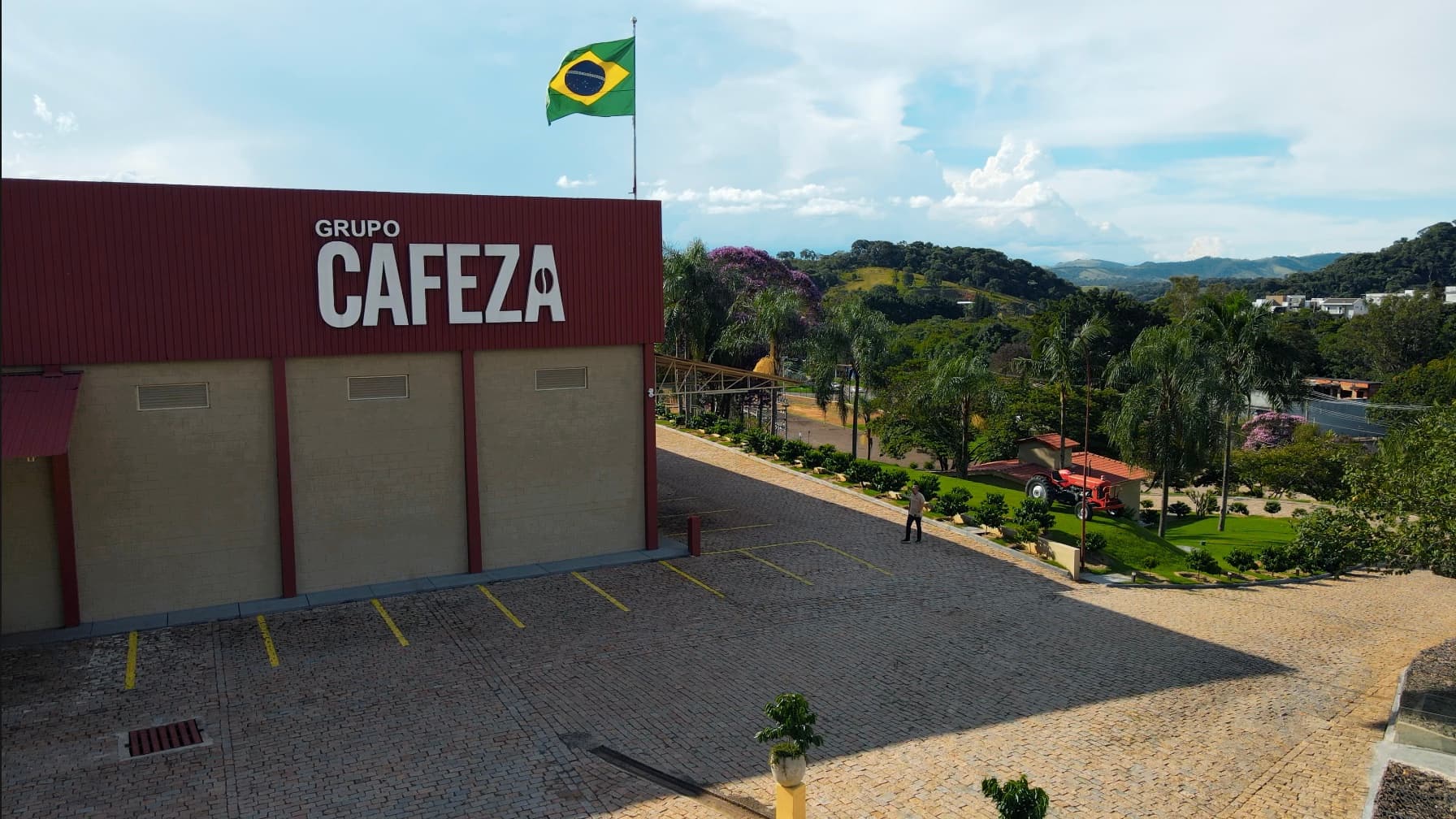 Fábrica da CAFEZA em Socorro-SP: o galpão com o letreiro Grupo CAFEZA, a bandeira do Brasil hasteada e as montanhas ao fundo